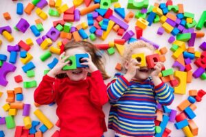 Happy preschool age children play with colorful plastic toy blocks. Creative kindergarten kids build a block tower. Educational toys for toddler or baby. Top view from above.