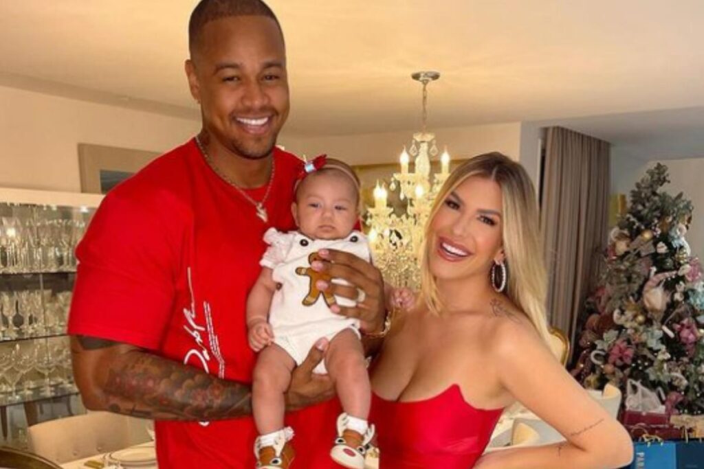 Bebe usando vestido rosa, perto do pai e mãe