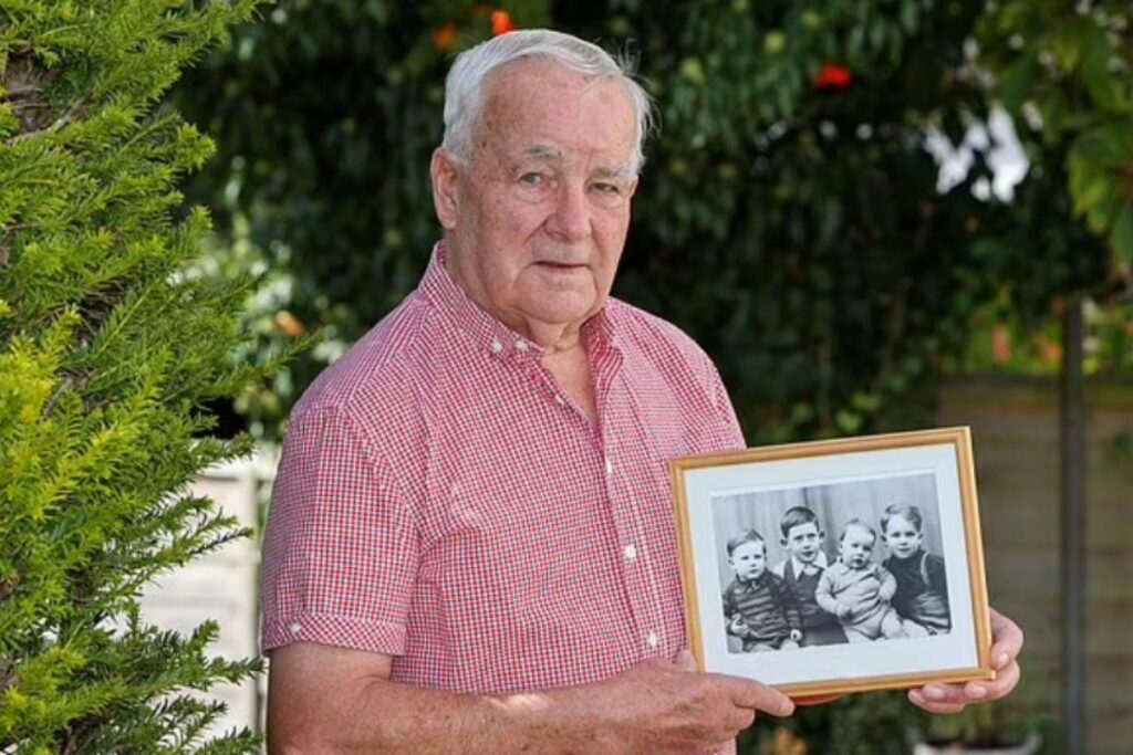 Geoff retratado com uma fotografia de si mesmo e seus irmãos três quando crianças