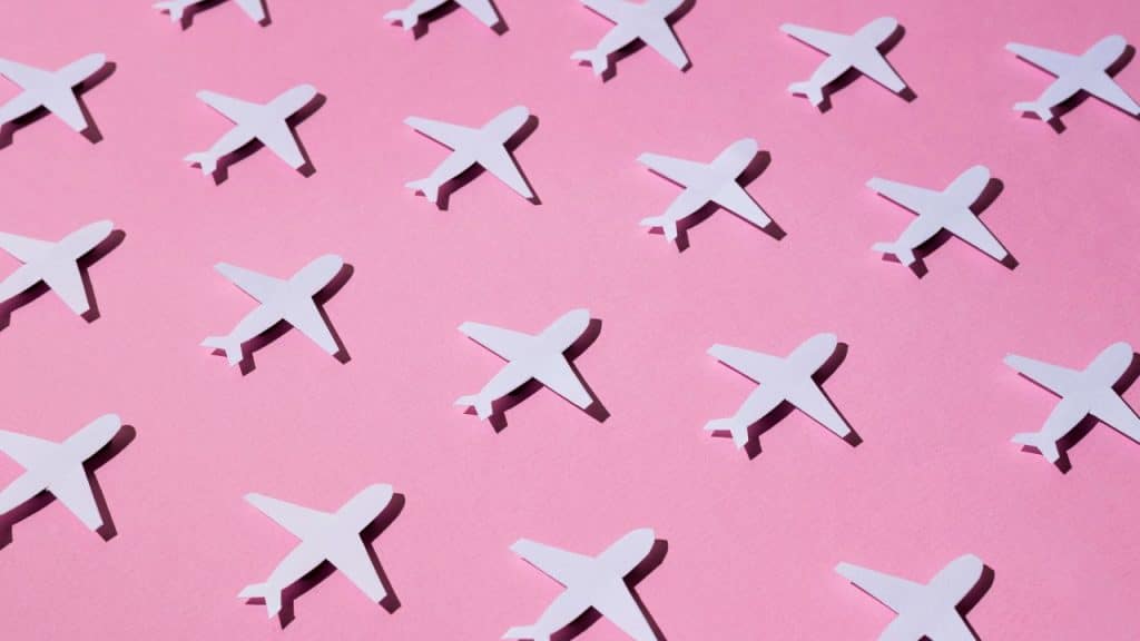 Aviões de papel em fundo rosa representando o jet lag.