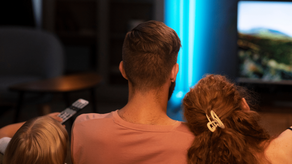 Um pai, uma mãe e um filho assistindo alguma coisa na televisão