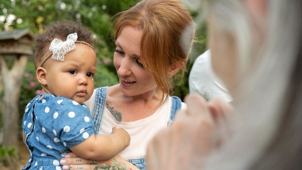 Bebê no colo da mãe olha desconfiado para uma pessoa idosa que se aproxima