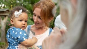 Bebê no colo da mãe olha desconfiado para uma pessoa idosa que se aproxima