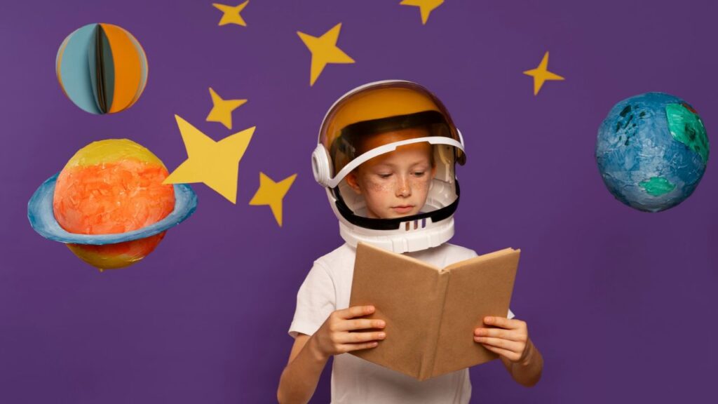 Menino com capacete de astronauta lendo um livro diante de uma parede roxa decorada com estrelas amarelas e planetas de papel machê. Criança não gosta de ler